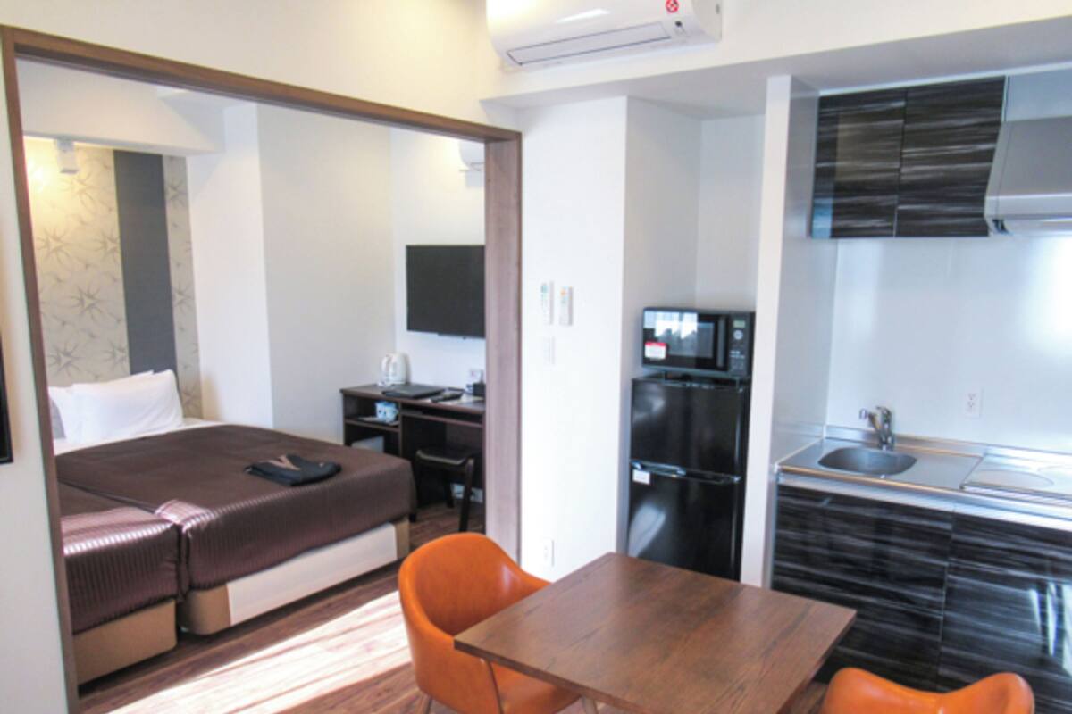 Une chambre d’hôtel compacte comprenant un lit, un bureau, une petite kitchenette et un coin repas avec deux chaises.