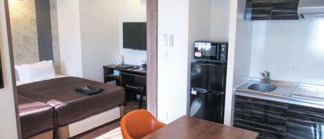 A compact hotel room with a bed, a desk, a small kitchenette, and a dining area with two chairs.