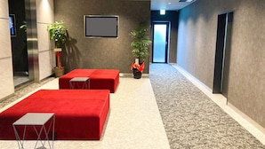 Un hall d’entrée moderne avec des sièges rouges, un grand écran et une plante.