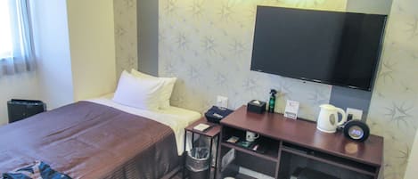 Hotellihuone, jossa on sänky, työpöytä, tuoli, televisio sekä pieni pöytä, jossa on vedenkeitin ja roskakori.