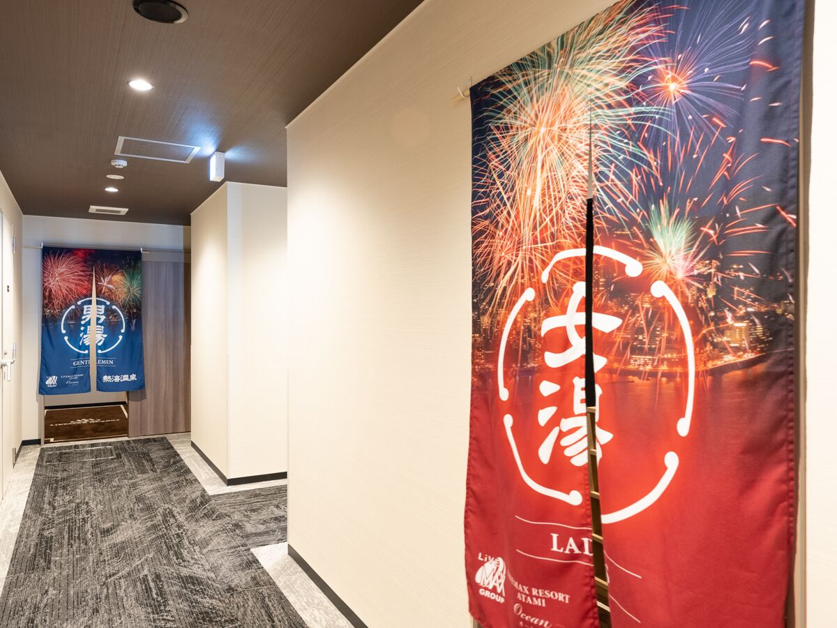 A hallway with a red banner featuring fireworks and Japanese characters, a blue banner with fireworks and text, and a wooden door at the end.