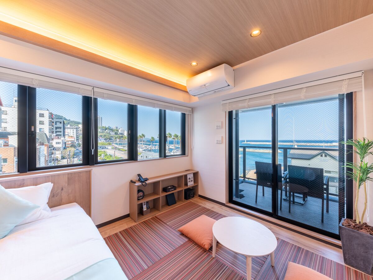 Habitación de hotel con cama, una mesita, sofá, televisor y balcón con vistas al mar.