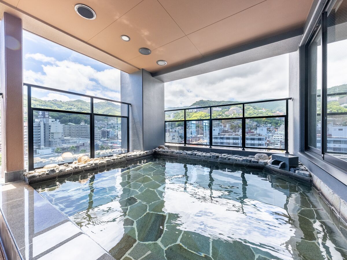 An indoor swimming pool with stone tiles, large windows, and a view of a cityscape.