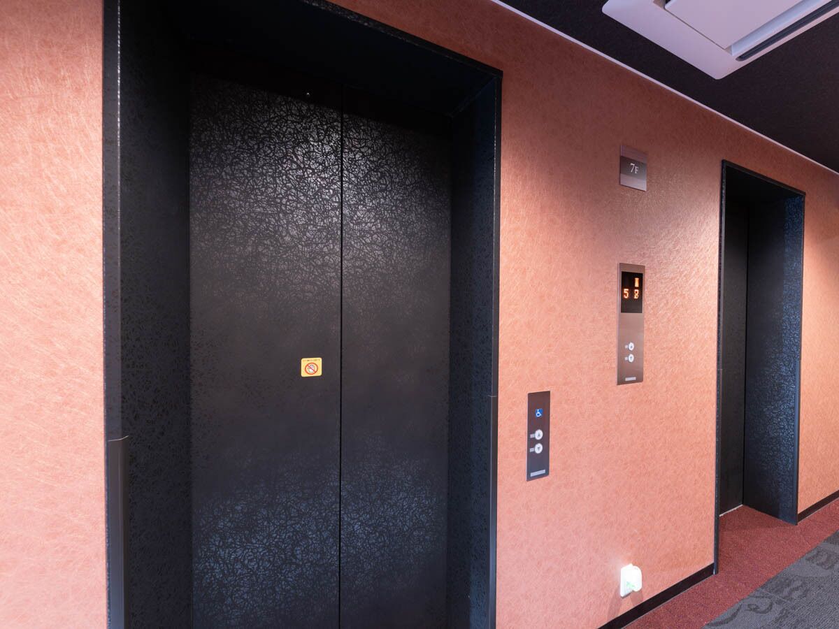 Un couloir avec deux portes d’ascenseur, dont l’une porte un panneau indiquant qu’il est interdit de fumer.