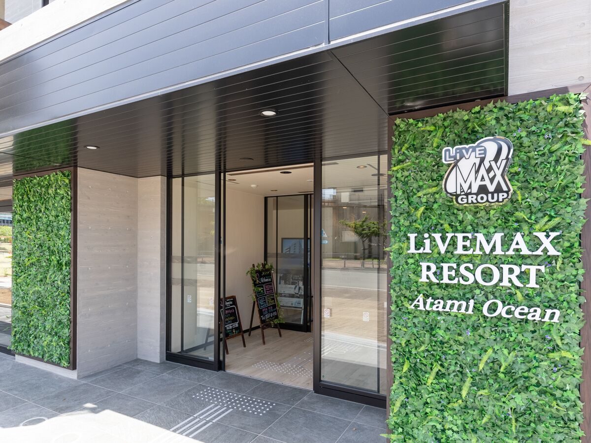 The exterior of Livemax Resort Atami Ocean with a modern design, featuring a glass entrance and a green vertical garden.