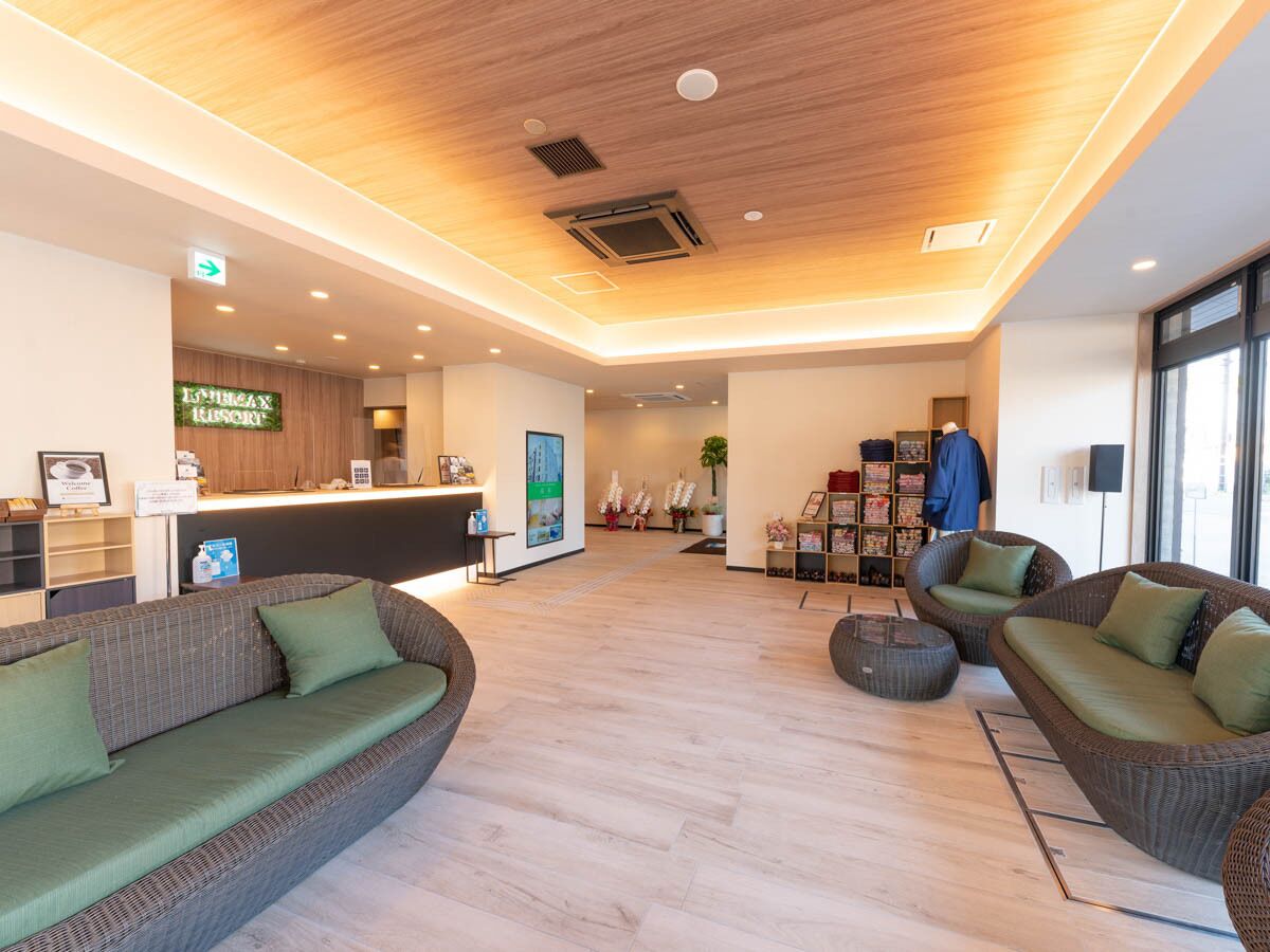 A modern lobby with a reception desk, wicker sofas, a bookshelf, and a wooden ceiling.