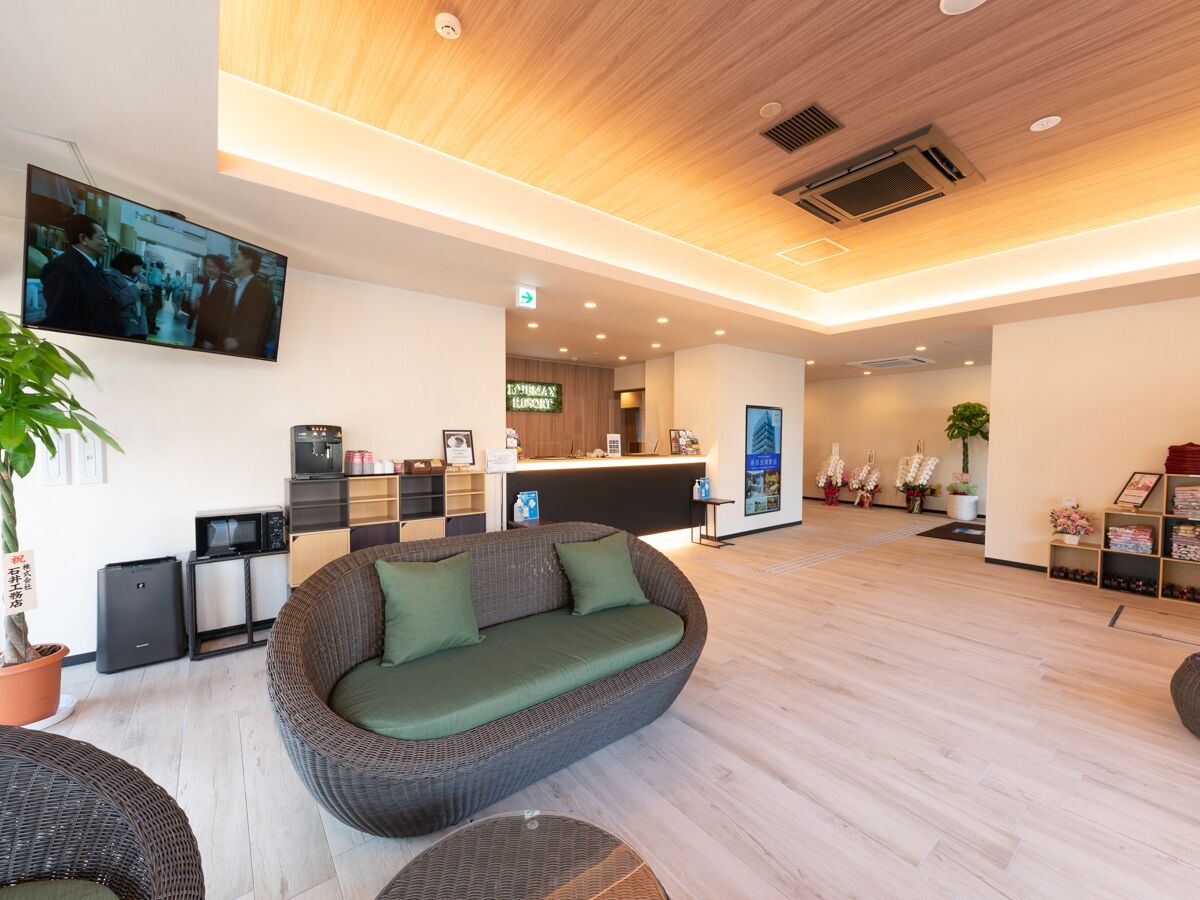 A modern hotel lobby with a reception desk, a large flat-screen TV, a sofa, and a coffee machine.
