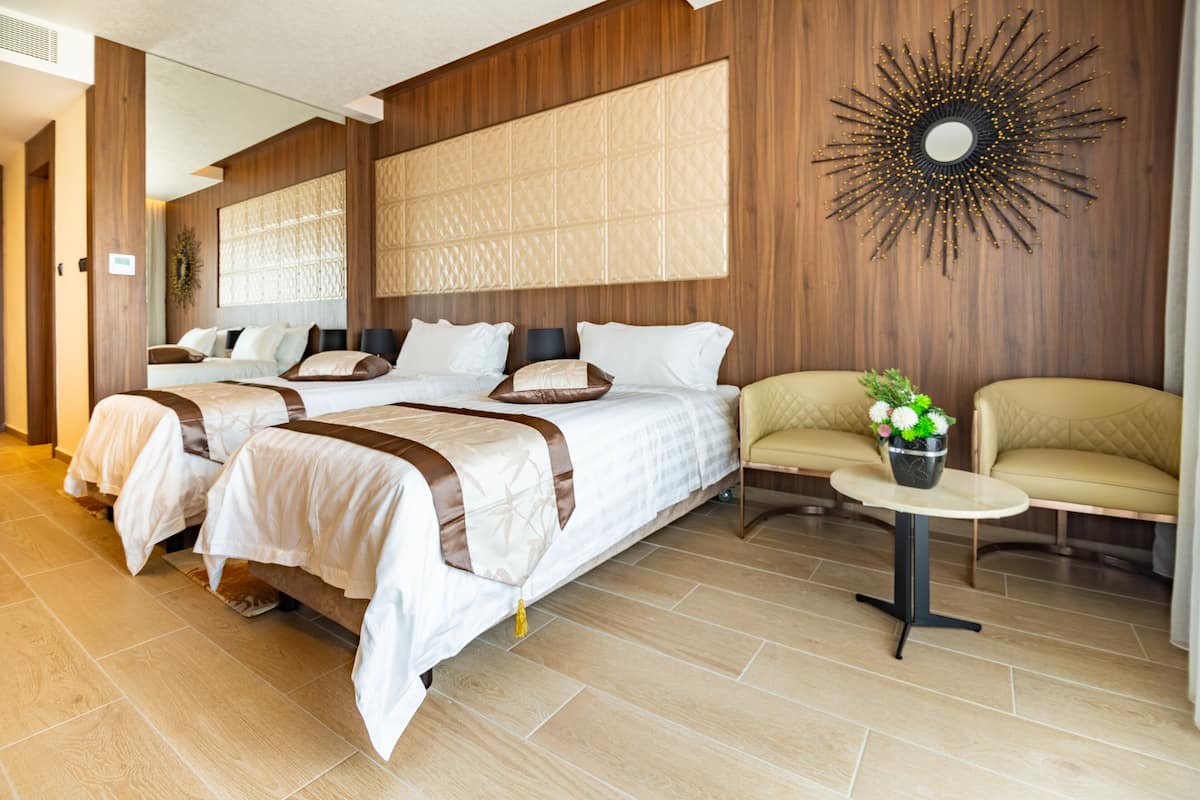 A hotel room with two beds, a sofa, a small table with a plant, and a decorative wall piece.
