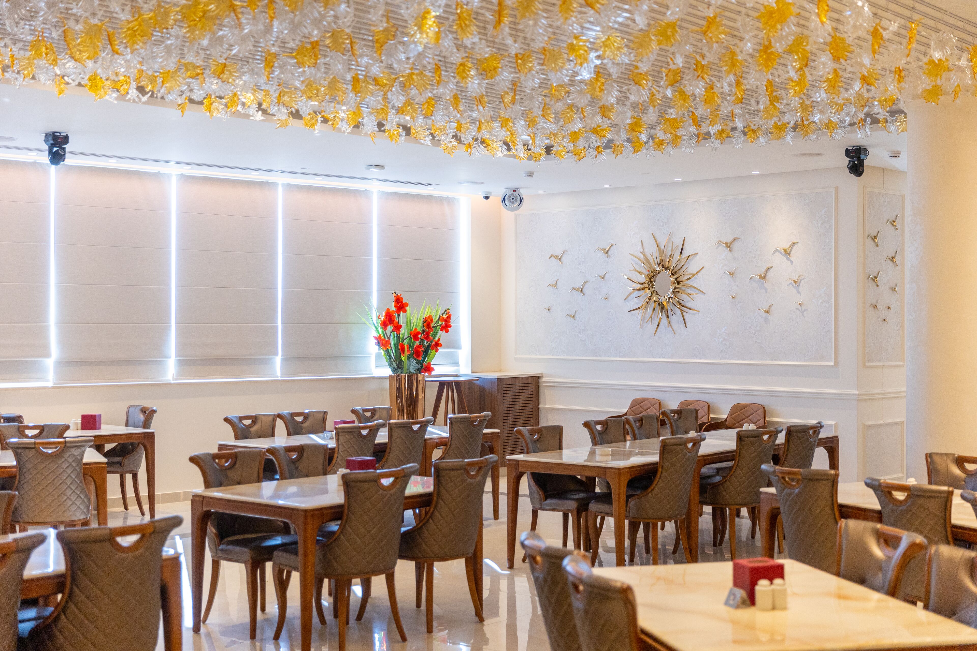 A dining area with multiple tables and chairs, a decorative ceiling, and a wall with a sunburst design.
