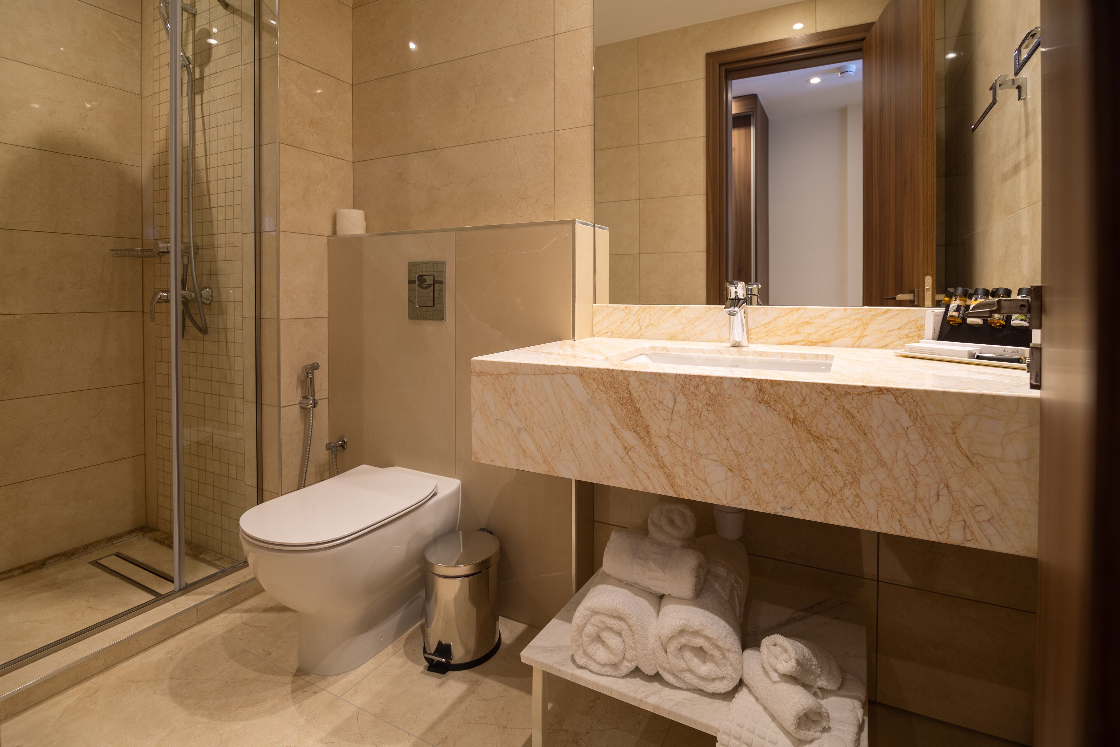 A modern bathroom with a glass-enclosed shower, a toilet, and a marble sink with a mirror above.