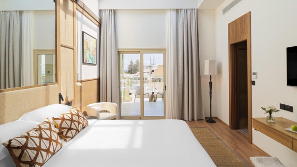 A hotel room with a large bed, a sitting area, a TV, and a balcony with a view of the city. - Leonardo Boutique Hotel Larnaca (Larnaca)