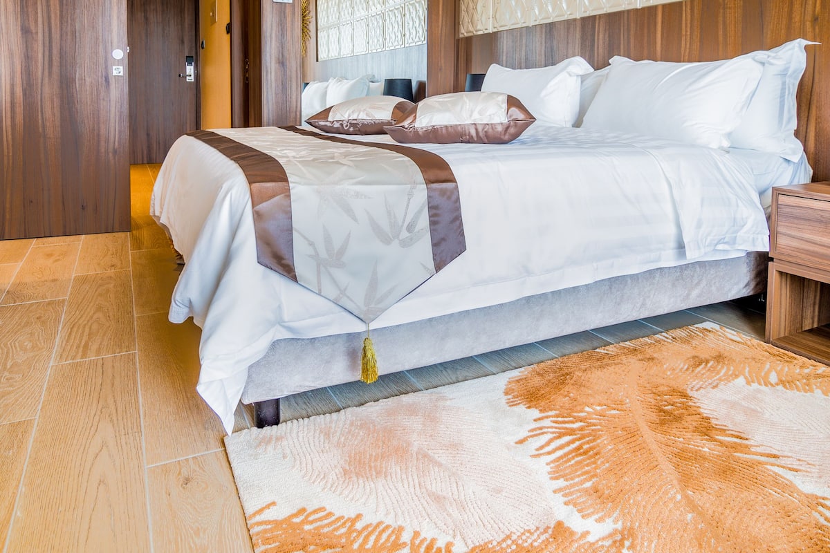 A modern hotel room with a large bed, wooden paneling, and a patterned headboard.