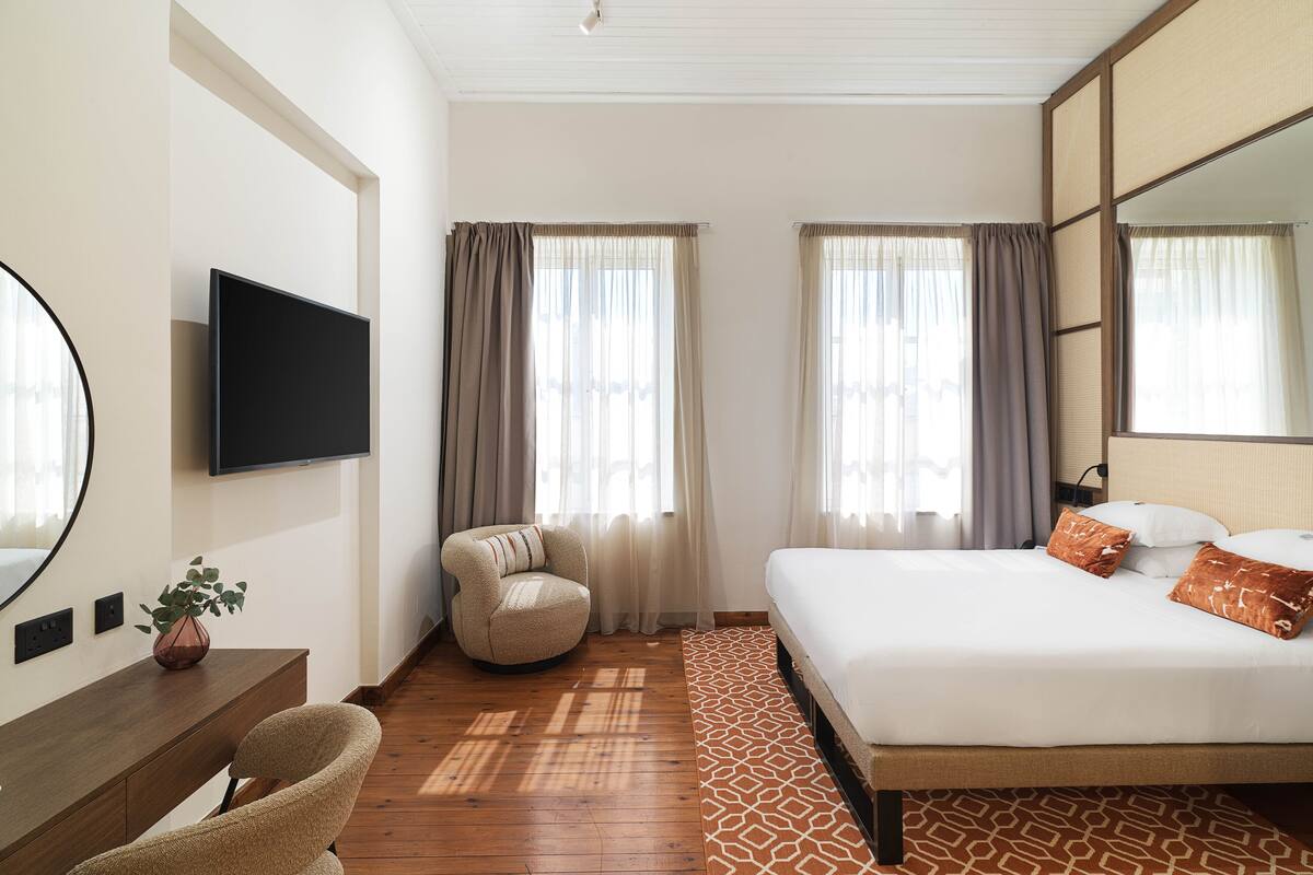 A hotel room with a bed, a desk, a chair, a TV, and a large mirror.