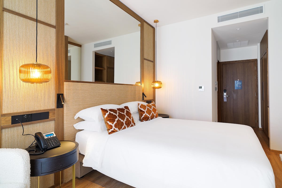 A hotel room with a large bed, a bedside telephone, a mirror, and a wooden headboard.