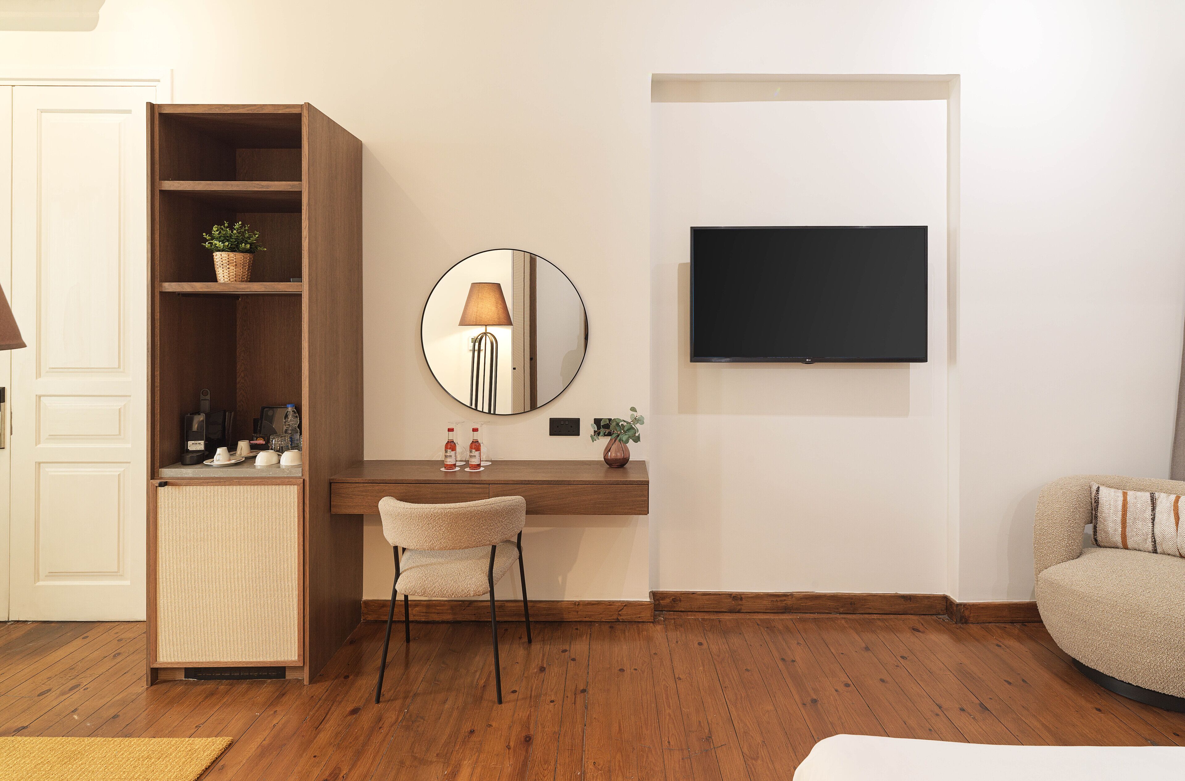 A modern living room with a wooden desk, a round mirror, a television mounted on the wall, and a sofa.