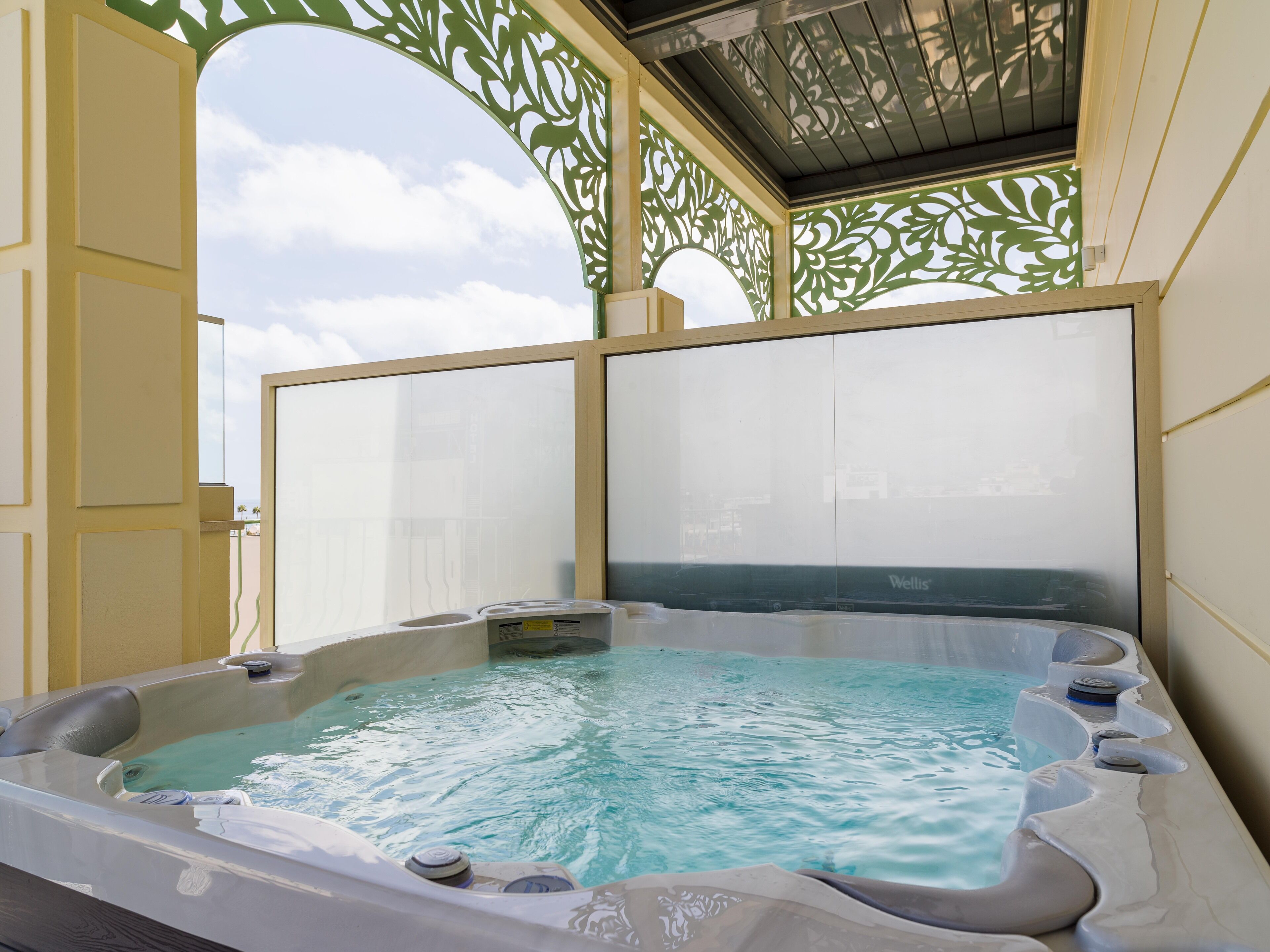 A hot tub with a clear view of the sky through a decorative screen, surrounded by a yellow wall and a wooden ceiling.