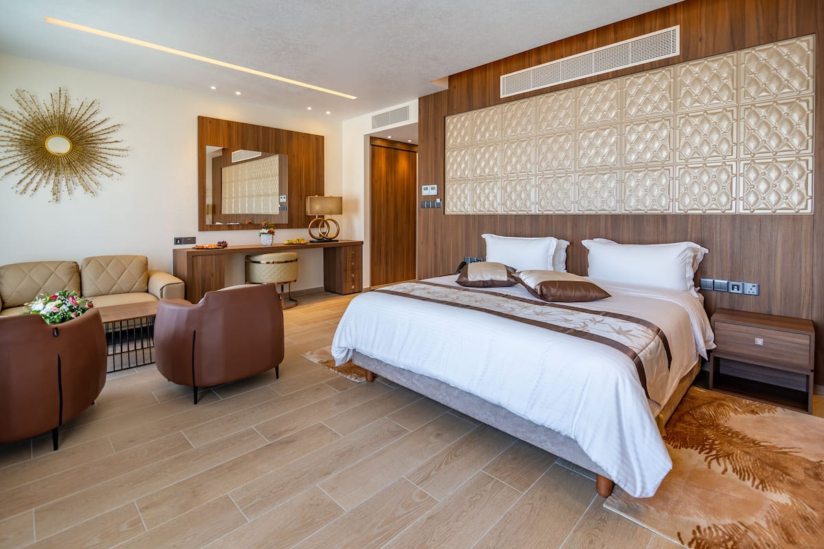 A modern hotel room with a large bed, a desk, a sofa, and a decorative wall panel.