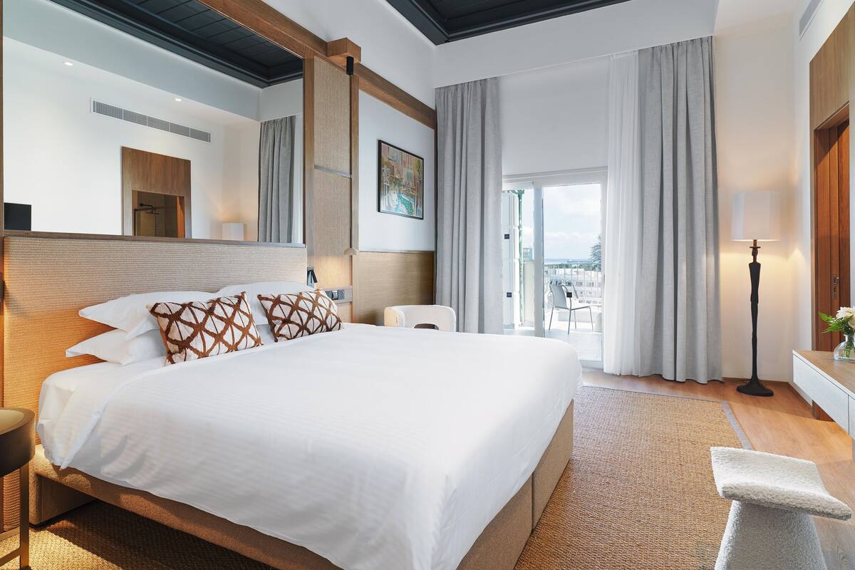 A modern hotel room with a large bed, a wooden headboard, a view of the city, and a balcony with a view.