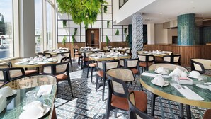 Un restaurante moderno con mesas redondas, sillas de mimbre y una planta verde colgante.