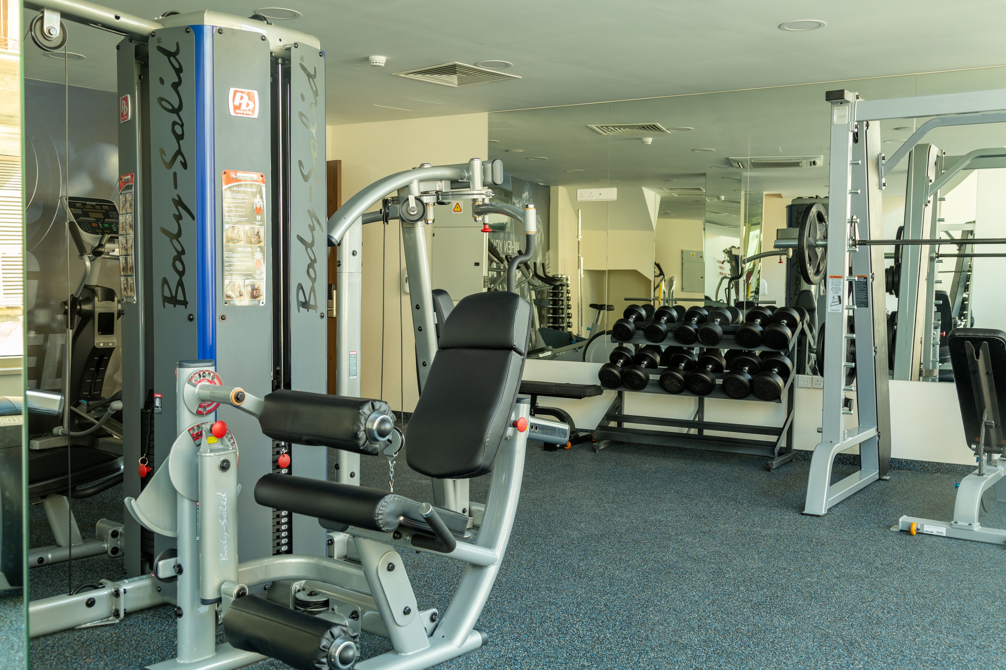 Uma academia com diversos equipamentos de exercícios, incluindo um banco de musculação, halteres e aparelhos de peso.