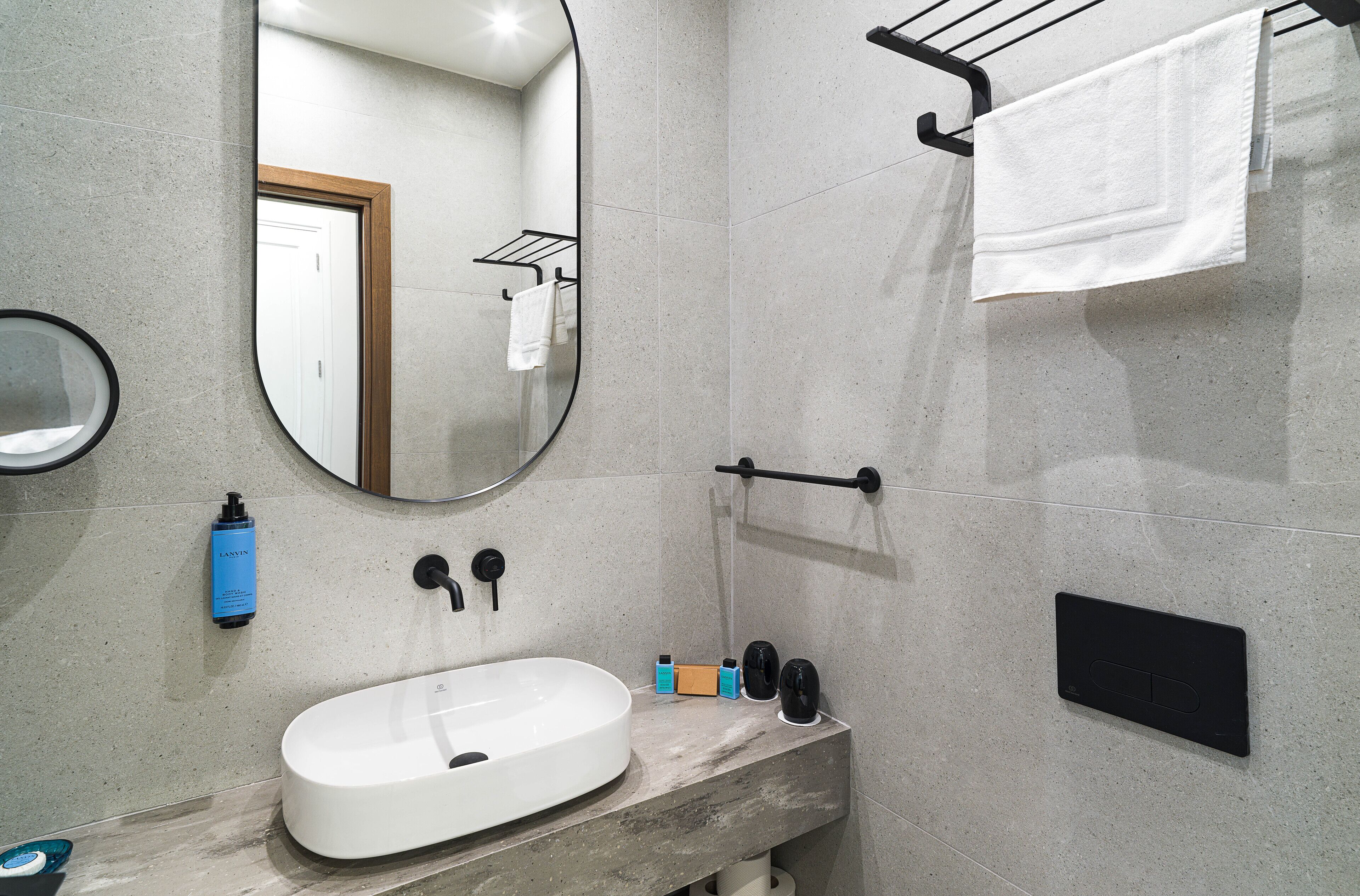 A modern bathroom with a large mirror, a sink, towel rack, and toiletries.