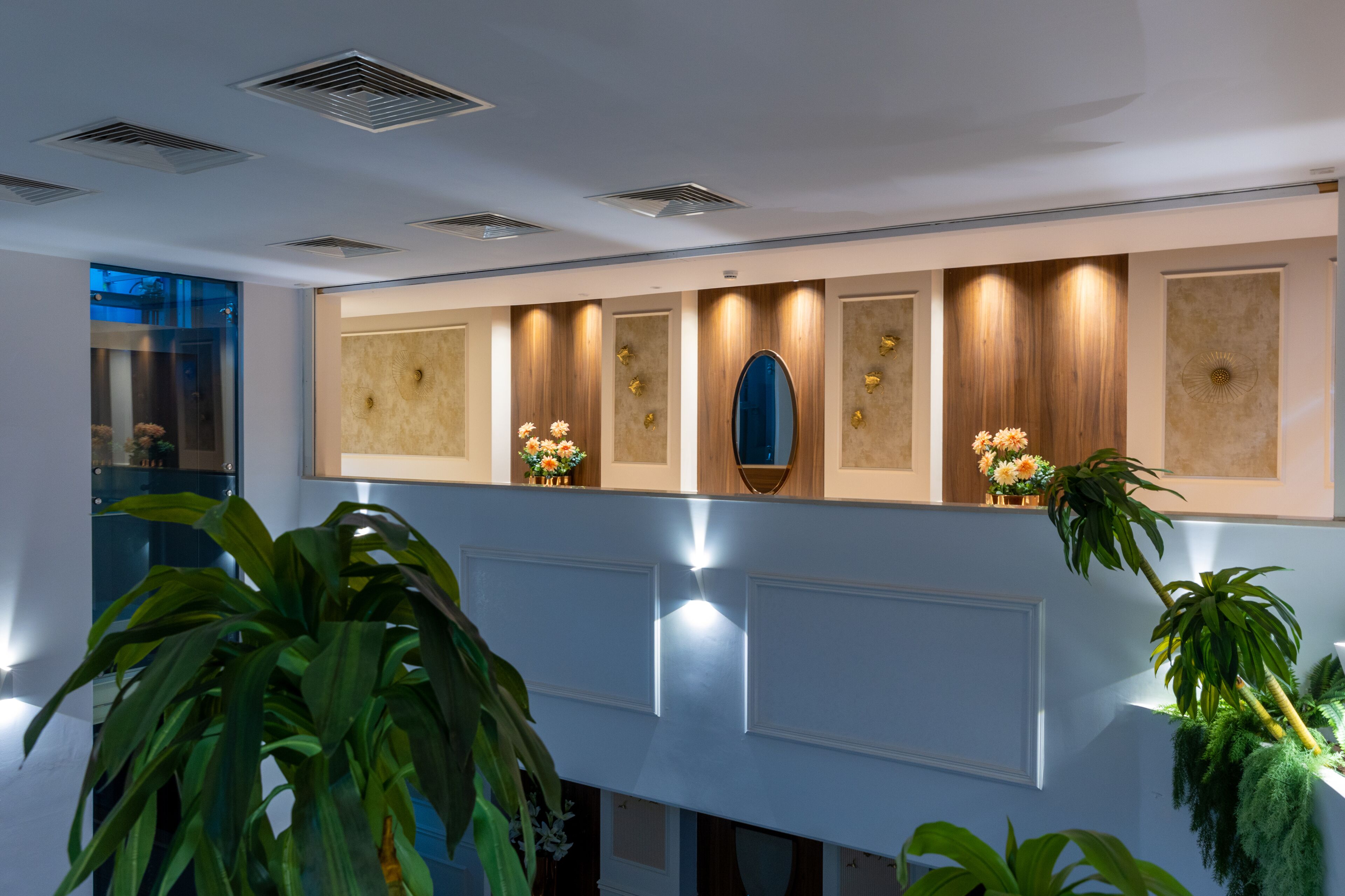 A modern lobby with a long reception desk, decorative wall panels, and potted plants.