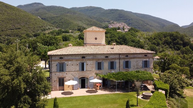A stone building with a tiled roof, a small tower, and a paved patio with umbrellas.