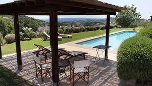 A covered patio with a pool, lounge chairs, and a view of the countryside.