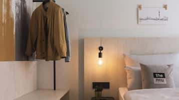 Ein ordentlich eingerichtetes Hotelzimmer mit einem Bett, einem Nachttisch mit Lampe, einem Kleiderhaken und einem Wandbild.