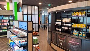 A modern interior with a counter displaying snacks and beverages, shelves with packaged goods, and a digital screen.