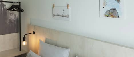 Un dormitorio con cabecera, lámpara de noche y dos almohadas. Hay dos cuadros en la pared.