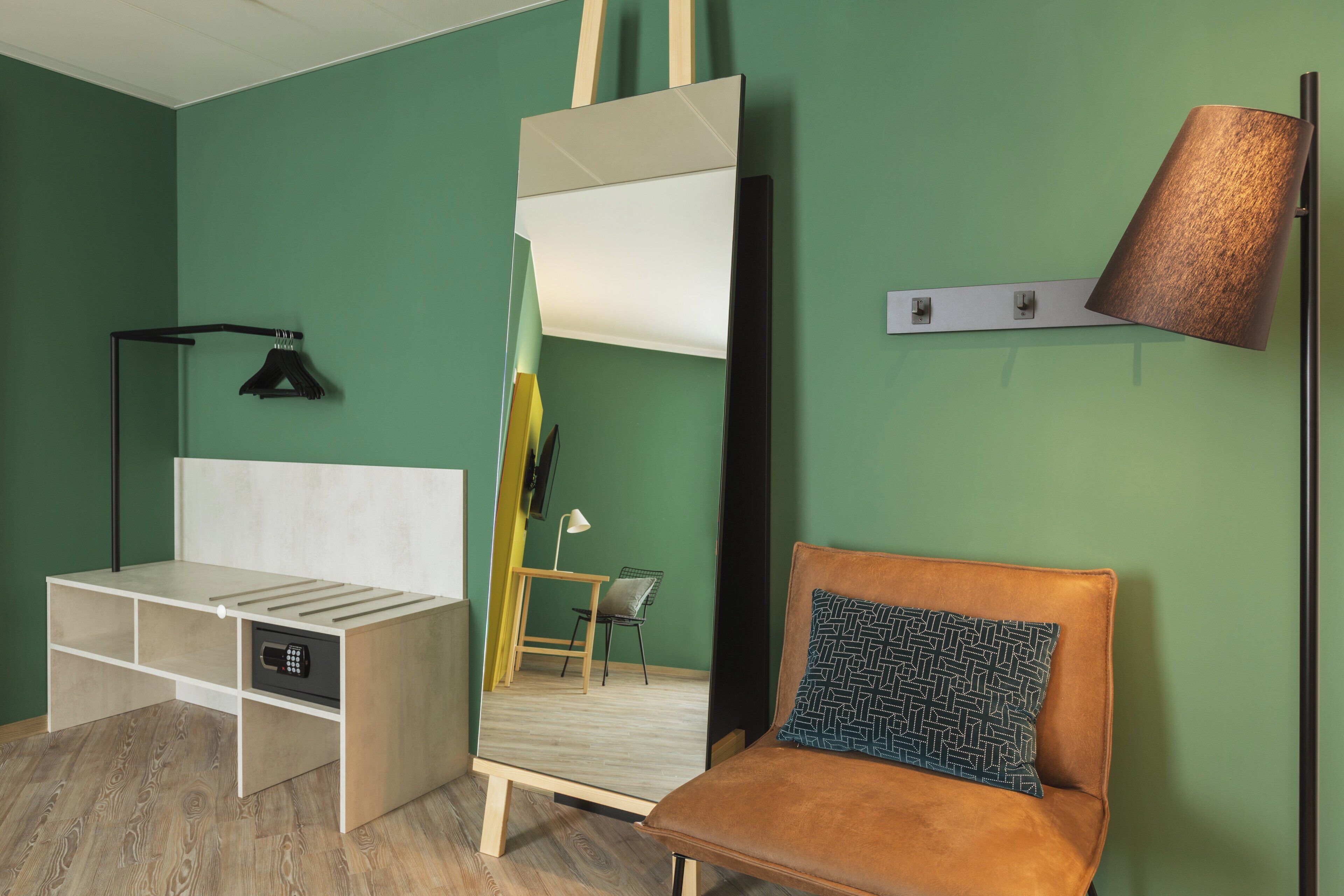 A room with a bed, a chair, a desk, a mirror, and a lamp.