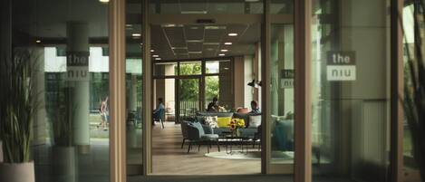 An entrance to a modern building with glass doors, a seating area with sofas and a coffee table, and a visible sign that reads "the niu".