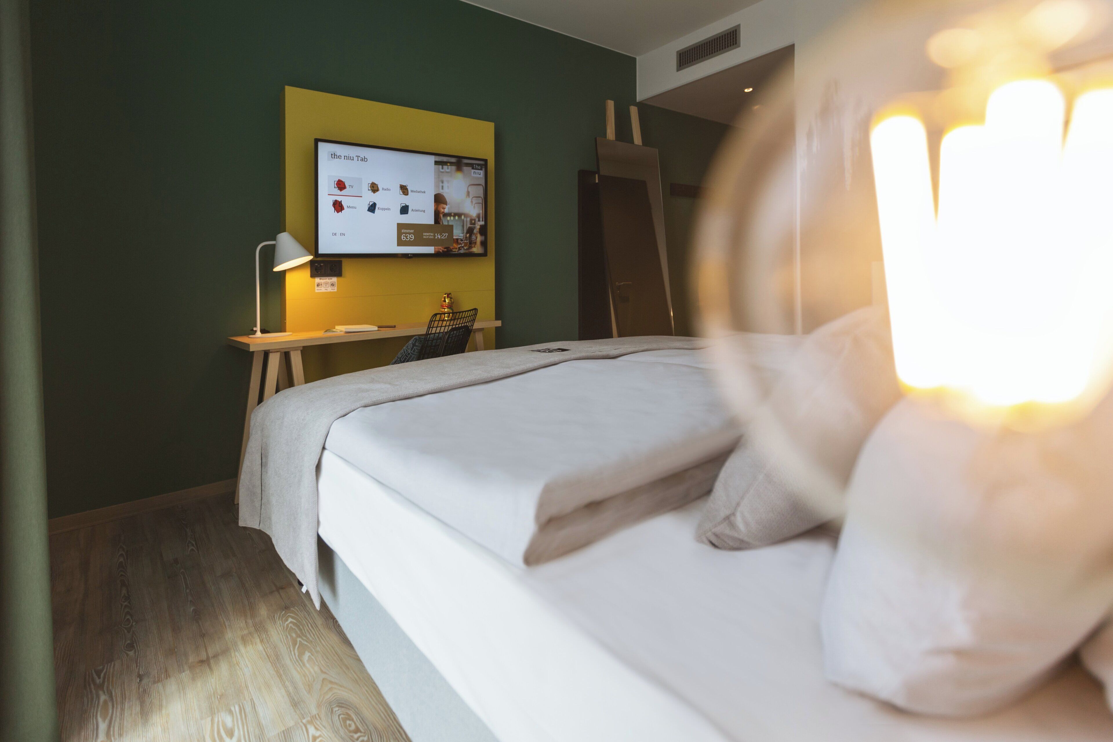Une chambre d’hôtel équipée d’un lit, d’un bureau et d’un téléviseur fixé au mur, qui affiche un menu.