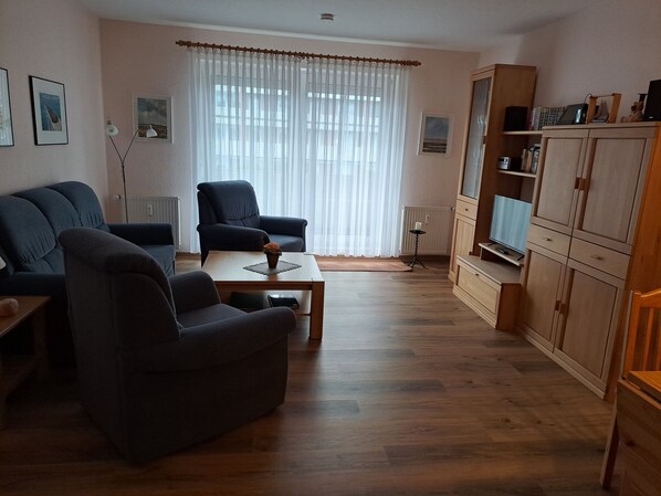 A living room with a sofa, armchairs, a coffee table, a TV, and wooden cabinets.
