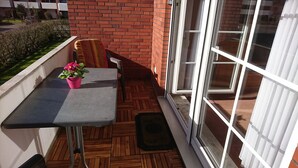 A balcony with a table, chairs, a potted plant, and a window. - Vacation apartment in Haus Borkum 1 upper floor plus visitor's tax (Dornum)