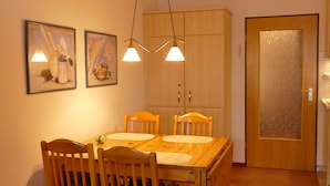 A dining area with a wooden table, four chairs, two pendant lights, and a cabinet with a frosted glass door. - Vacation apartment in Haus Borkum 1 upper floor plus visitor's tax (Dornum)