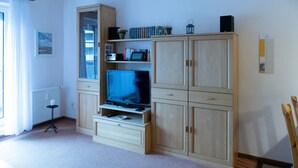 A room with a television on a wooden cabinet, a radiator, and a small table with a candle. - Vacation apartment in Haus Borkum 1 upper floor plus visitor's tax (Dornum)