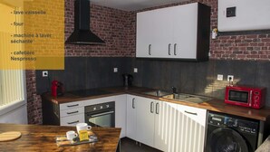 A compact kitchenette with a brick wall, a black range hood, a white cabinet, a red microwave, and a washing machine. - Meublé de Tourisme 3 Loft Industriel à Fismes (Fismes)