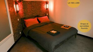 A bedroom with a brick wall, a bed with dark bedding, and two wall-mounted lights. - Meublé de Tourisme 3 Loft Industriel à Fismes (Fismes)