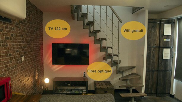 A living room with a TV, a staircase, and a sign indicating free WiFi. - Meublé de Tourisme 3 Loft Industriel à Fismes (Fismes)