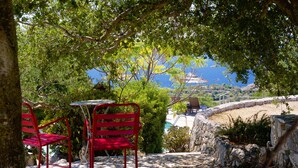 Un patio con una mesa y dos sillas rojas, con vista a un paisaje que incluye una masa de agua y colinas.