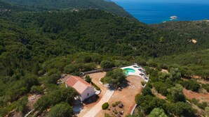 Vista aérea de una propiedad con piscina, una casa de techo rojo y un paisaje boscoso.