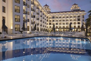 Un hotel con una piscina amplia, varios balcones y sillones de descanso.