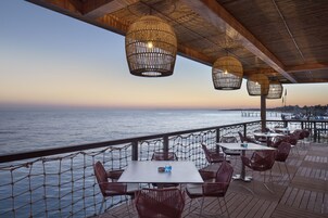 Un área de comedor al aire libre con mesas y sillas, con vista a una masa de agua.