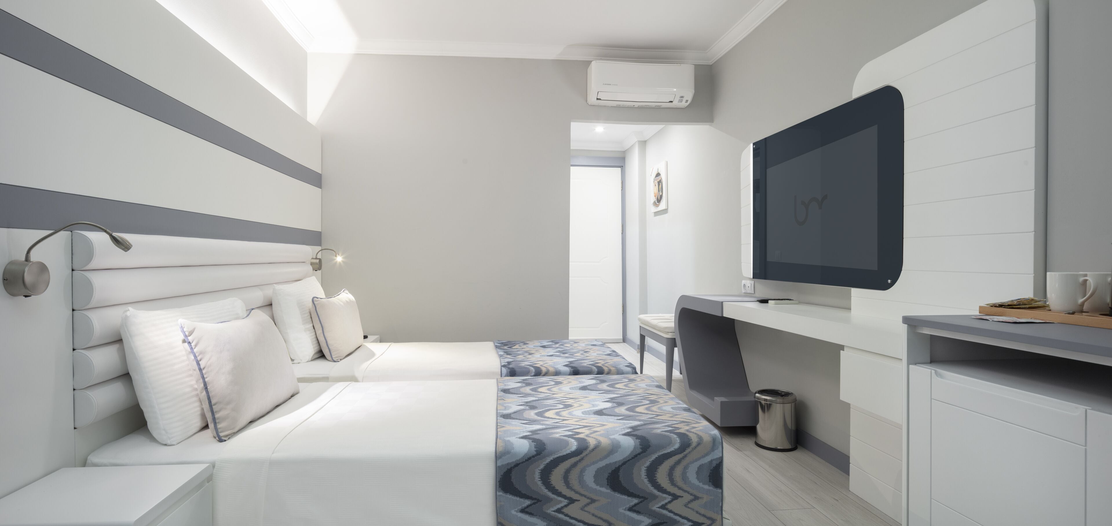 Ein modernes Hotelzimmer mit einem Bett, Nachttisch und einem an der Wand befestigten Fernseher.