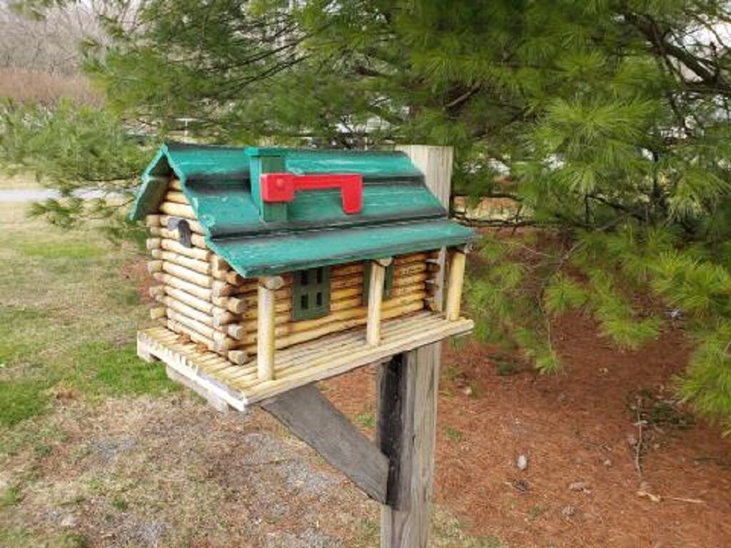 Een houten vogelhuisje met een groen dak en een rode sluiting, bevestigd aan een houten paal.