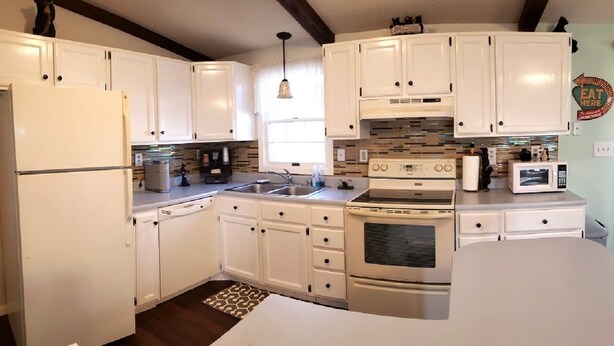 Una cocina compacta con armarios blancos, horno integrado, microondas y lavamanos.