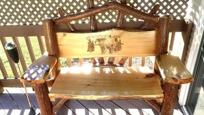 Un banco de madera con figuras de animales talladas en el respaldo, situado en una terraza de madera con un enrejado en el fondo.