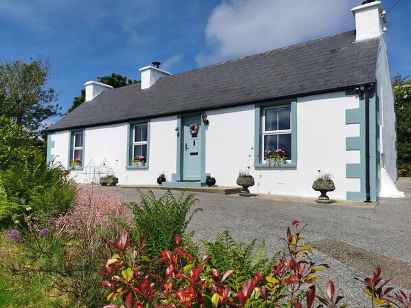 A white building with blue trim and a grey roof, surrounded by greenery and flowers. - 🐞New Listing🐞 Ladybird Cottage🐞Donegal - Wild Atlantic Way (Dunkineely)